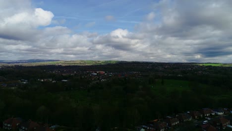 rising drone shot in bolton, england. show housing in the fore ground and hills and pasture in the background on a sunny day with blue sky