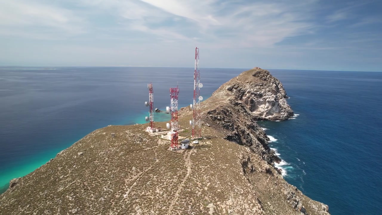 Torri cellulari su una collina costiera che si affaccia su un vasto oceano blu sotto un cielo limpido e soleggiato