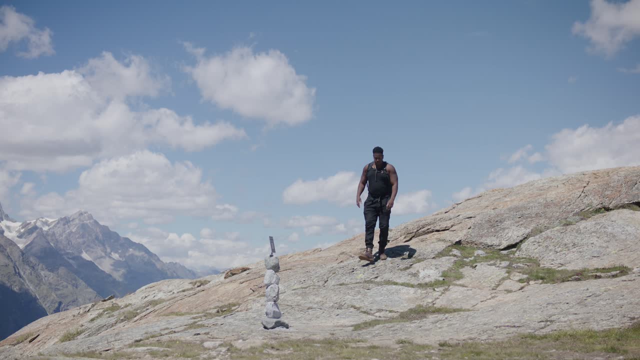 viajero masculino negro con mochila levantándose y caminando a lo largo de la escénica ladera de la montaña cerca del matterhorn en suiza