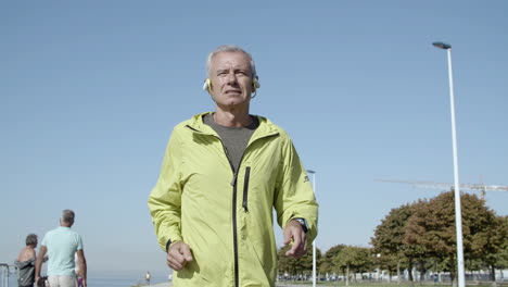 active male pensioner in headphones jogging outside