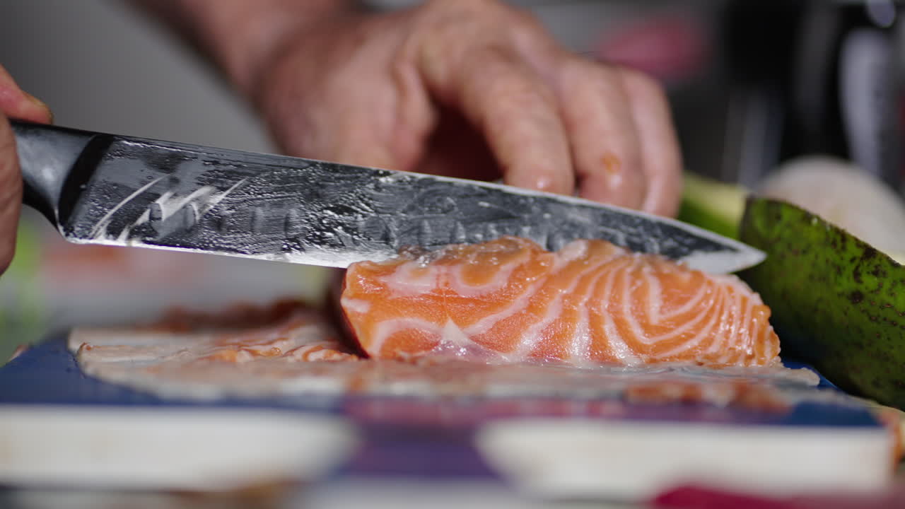Medium shot of hands cutting fresh salmon with a knife in a kitchen, indoor
