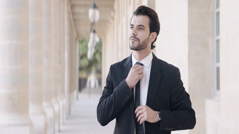 businessman adjusting tie in colonnade