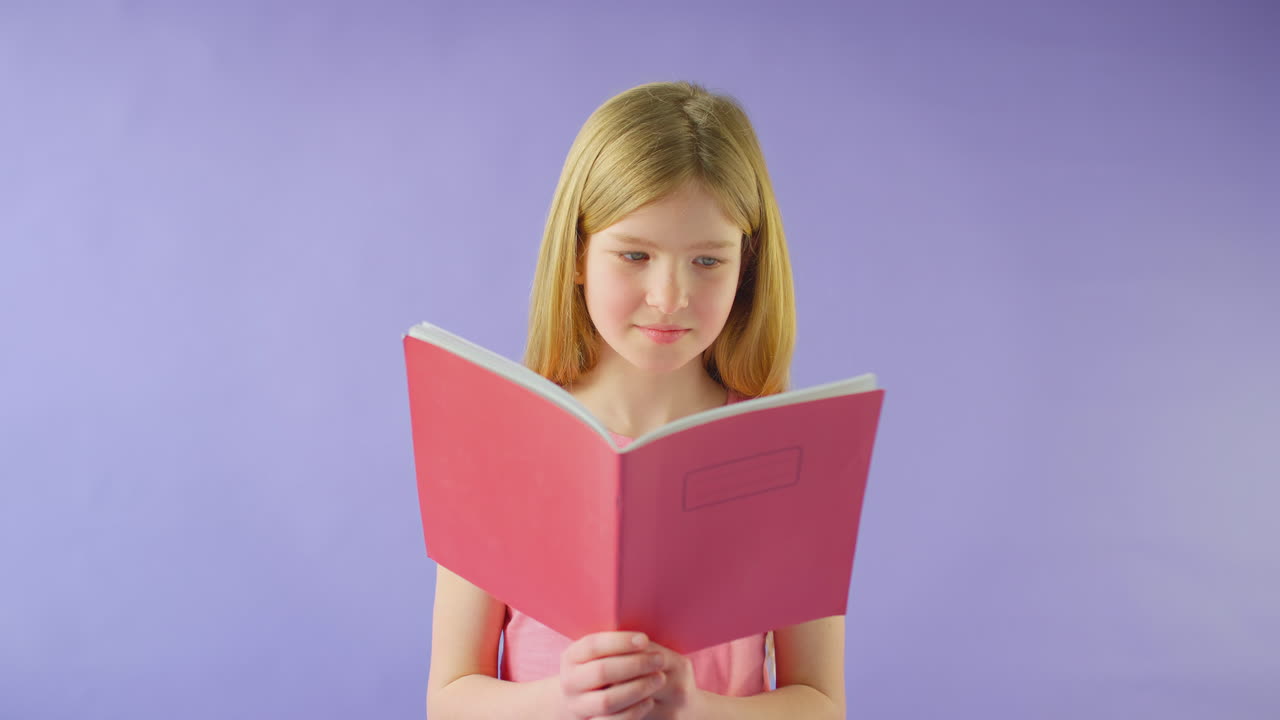Scatto in studio di giovane ragazza che studia un quaderno scolastico su sfondo viola