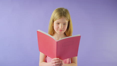 fotografía de estudio de una niña estudiando el libro de ejercicios escolar contra un fondo púrpura