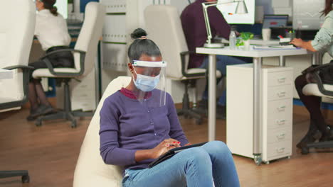 Black-businesswoman-with-mask-against-covid19-working-on-armchair