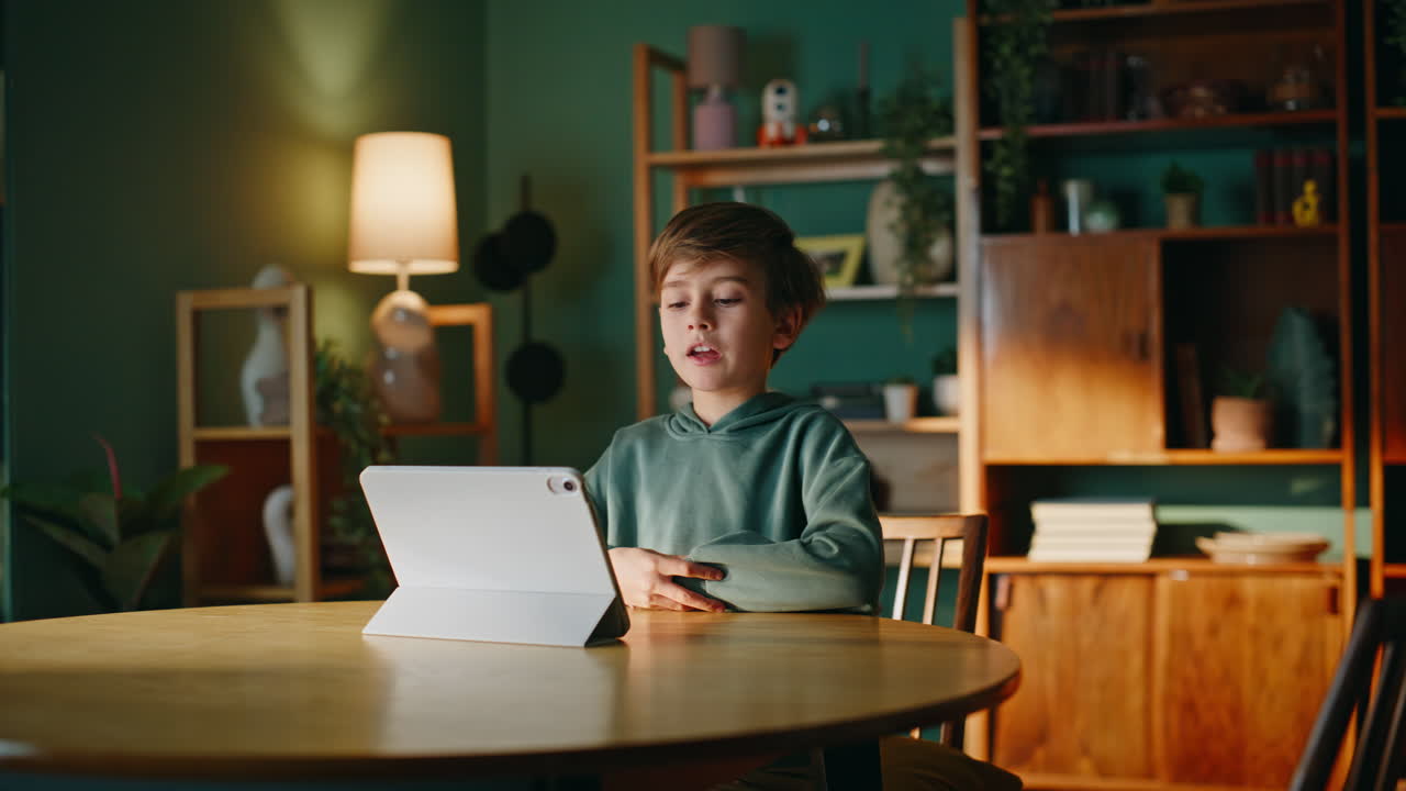 Schoolboy greeting online meeting waving hand to tablet camera closeup