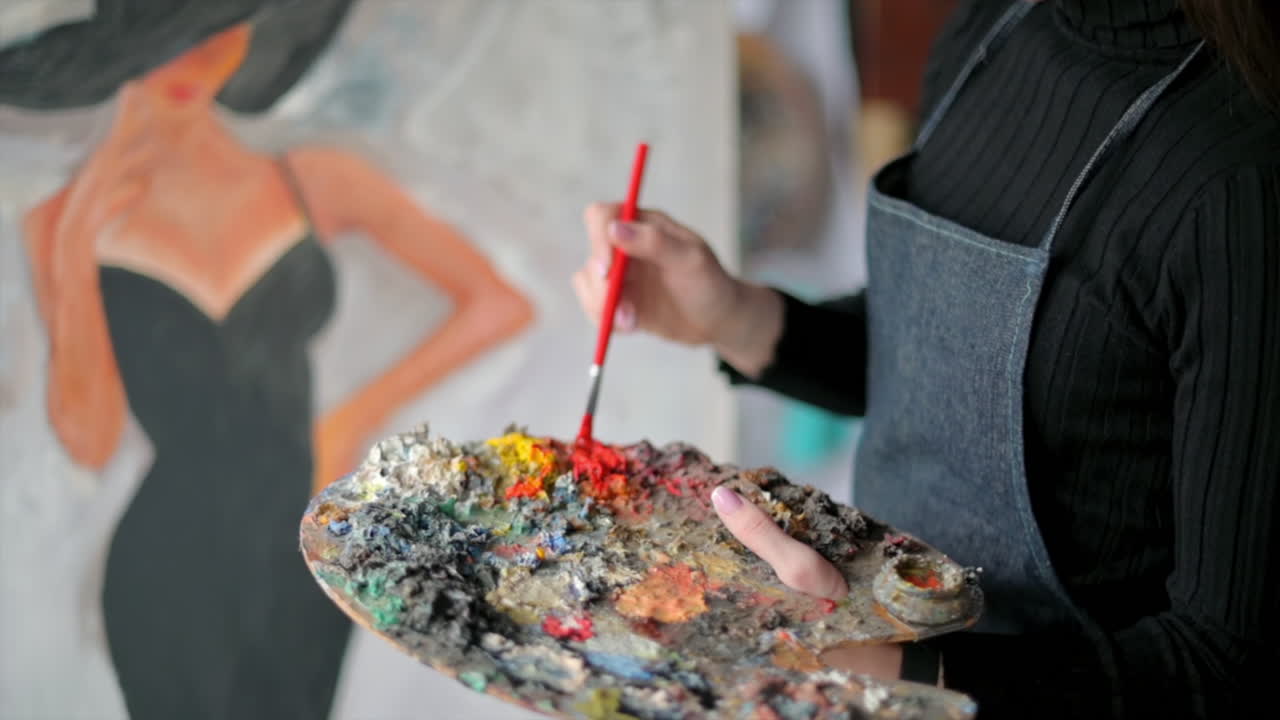 Woman painter wearing black clothes painting woman model face with hat drawing with red brush at a workshop