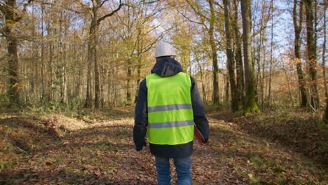 male engineer walking alone in the forest while carrying clipboard in safety vest to survey for trees, handheld following