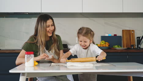 chica divertida rueda la masa con un alfiler de madera cocinando con mamá