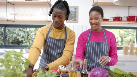 happy african american couple in aprons preparing meal in kitchen, slow motion