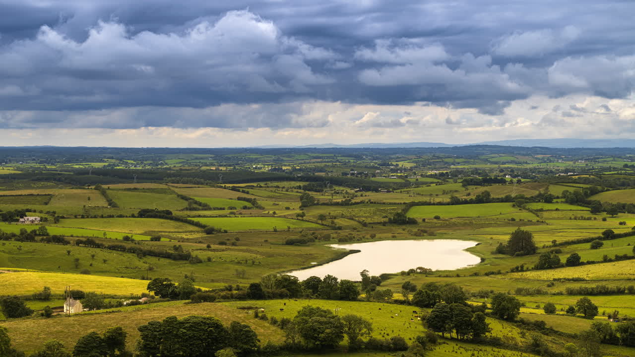 lapso de tiempo del paisaje agrícola rural con campos de hierba, lago y colinas durante un día nublado en irlanda