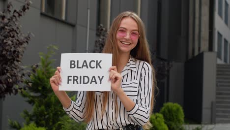 Joyful-teen-girl-showing-Black-Friday-inscription,-smiling,-looking-satisfied-with-low-prices