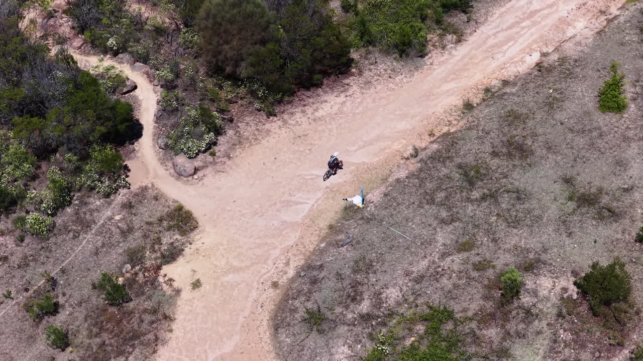 Ripresa aerea dall'alto segue un ciclista che percorre un sentiero sterrato tortuoso attraverso il bushland australiano