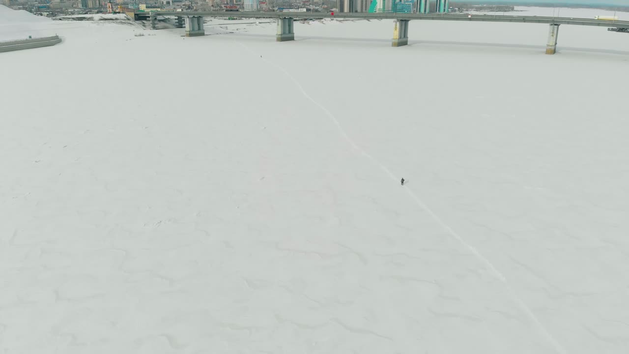 사람 실루엣이 얼어붙은 강 위의 눈 덮인 길을 따라 걷는다