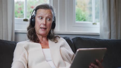 senior caucasian woman sitting wearing headphones and talking during video call using tablet