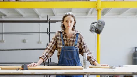 soldadora de pie con una tabla de madera en el taller 4k