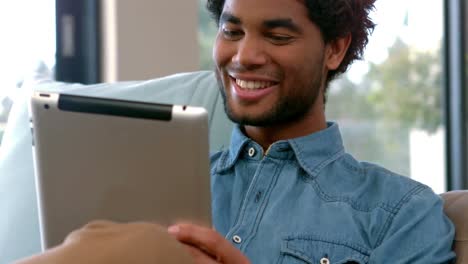 Handsome-man-using-his-tablet-pc-relaxing-on-his-sofa