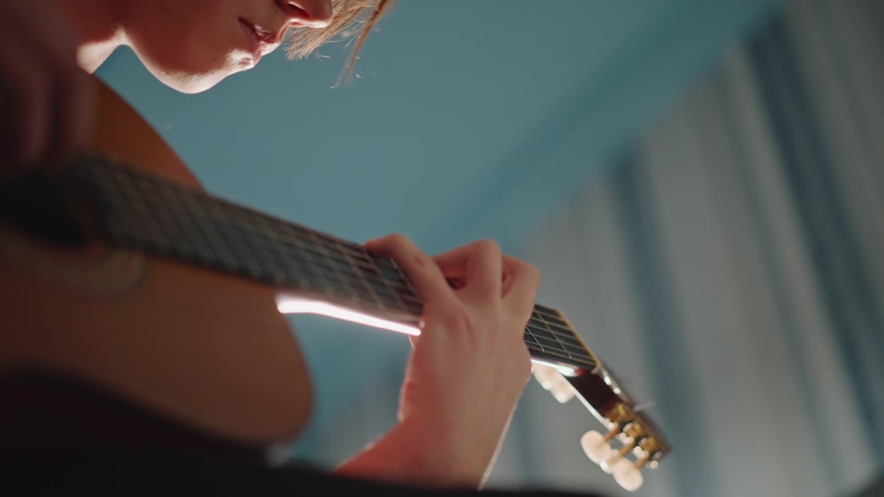 Guitar practice scene. Student rehearses intricate guitar passage. Focused player practicing challenging guitar segment indoors. Student rehearses detailed acoustic guitar piece in dimly lit room