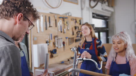 multi-cultural team of trainees in workshop learn how to assemble hand built bicycle frame together