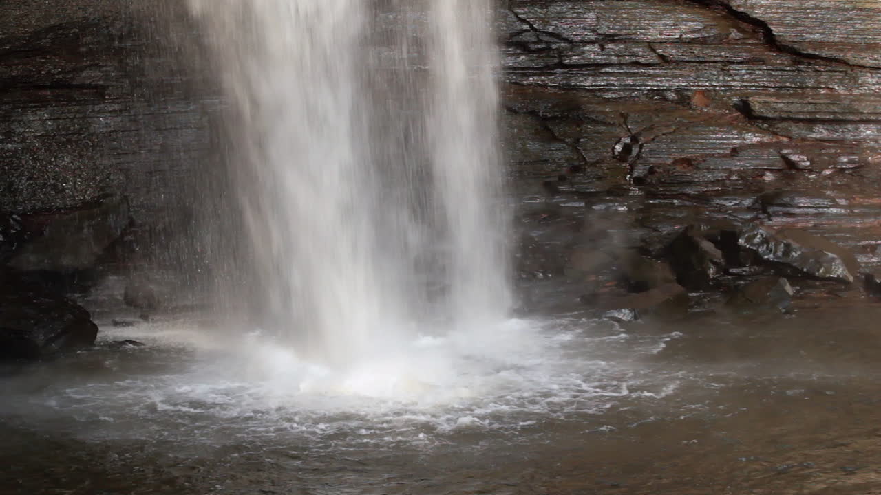 절벽 위로 흐르는 폭포의 타이트한 샷과 그 바닥에 있는 웅덩이로 튀는