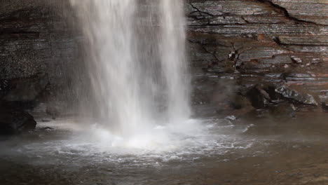 Tight-shot-of-a-waterfall-flowing-over-a-cliff-and-splashing-into-a-pool-at-it's-base