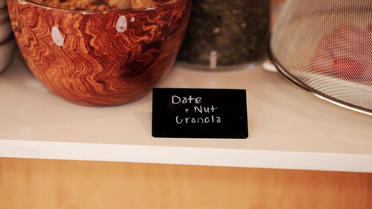 Lille tavle ved en morgenmadsbuffet med teksten "dadel- og nøddegranola" skrevet på den.