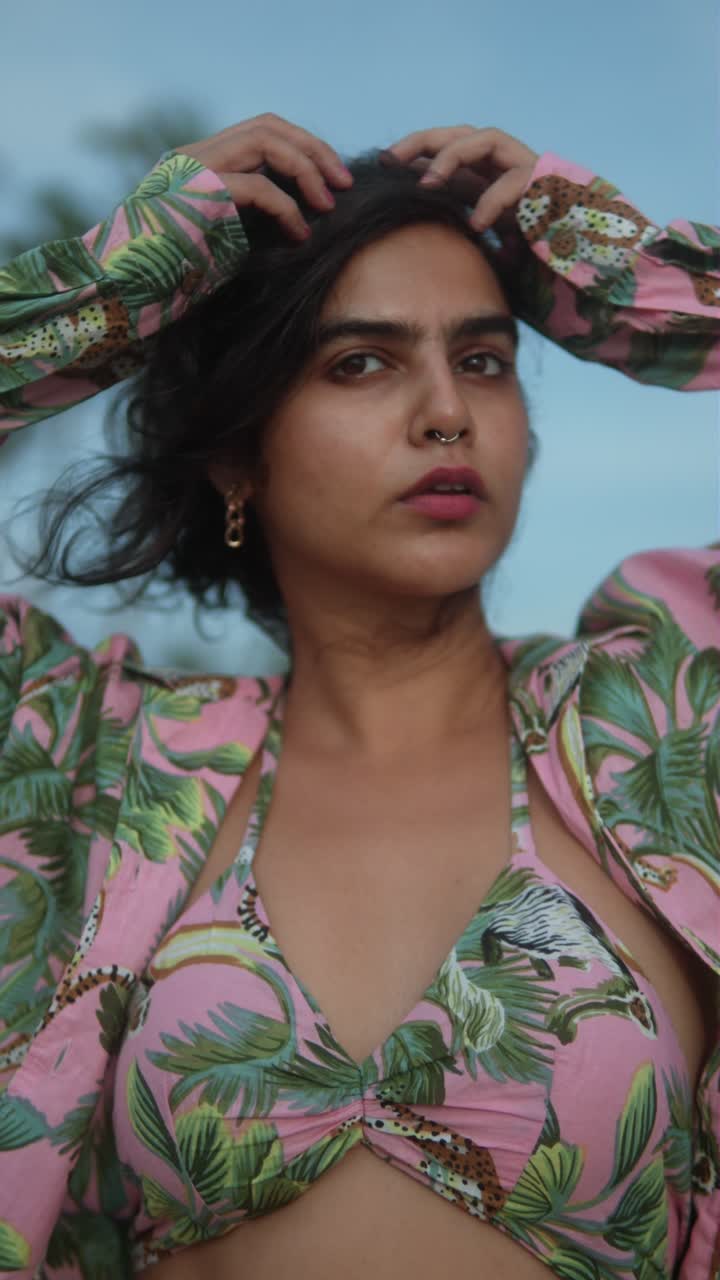 Woman in a colorful top looks confidently at the camera outdoors on a bright sunny day, vertical shot