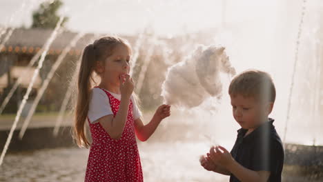 Little-boy-looks-at-cotton-candy-girl-eats-dessert-in-park