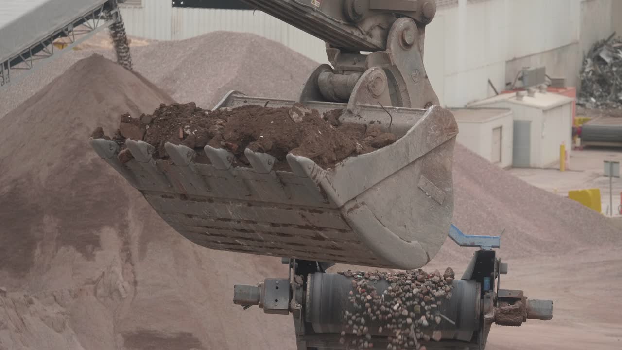Digger dropping soil and concrete into a recycling bin for processing