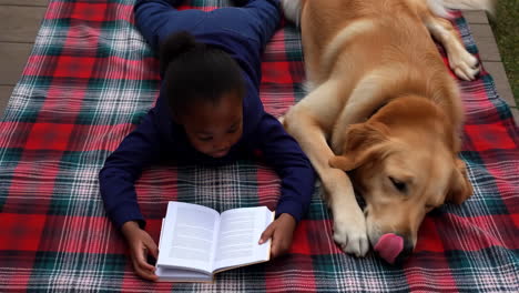child reading a book with a golden retriever on a plaid blanket