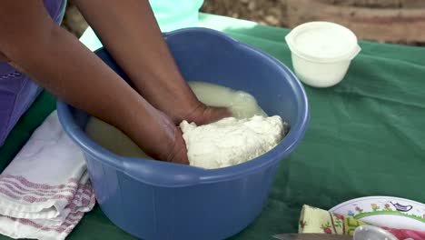 Indigenous-woman-from-Costa-Rica-pressing-curds-in-bucket-for-extracting-cheese-ball,-Close-up-handheld-shot