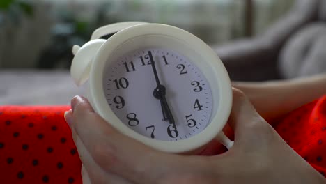 the woman sets the time on the alarm clock at 6 o'clock, and sets the alarm for the morning.