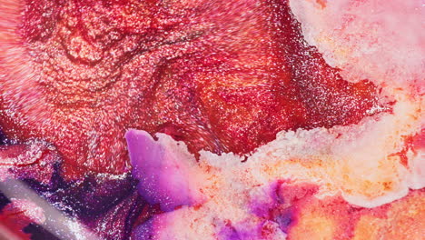 close-up of vibrant purple, orange, pink, and gold inks swirling in water. fluid motion and sparkling textures dominate the frame