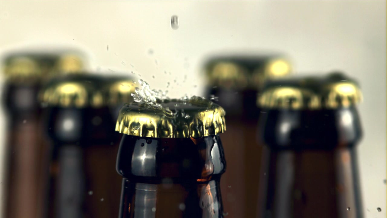 Gocce d'acqua che schizzano su tappi di bottiglia di birra dorati al rallentatore