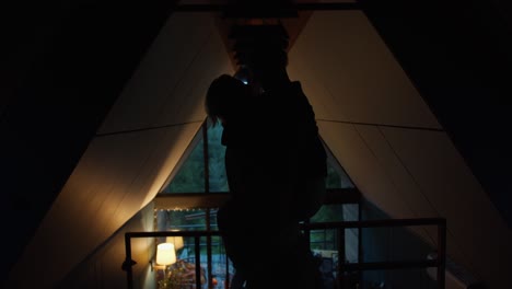 Silhouettes-of-a-guy-and-a-girl-are-hugging-against-the-background-of-a-window-overlooking-a-green-mountain-forest-in-a-dark-room.-romantic-meeting