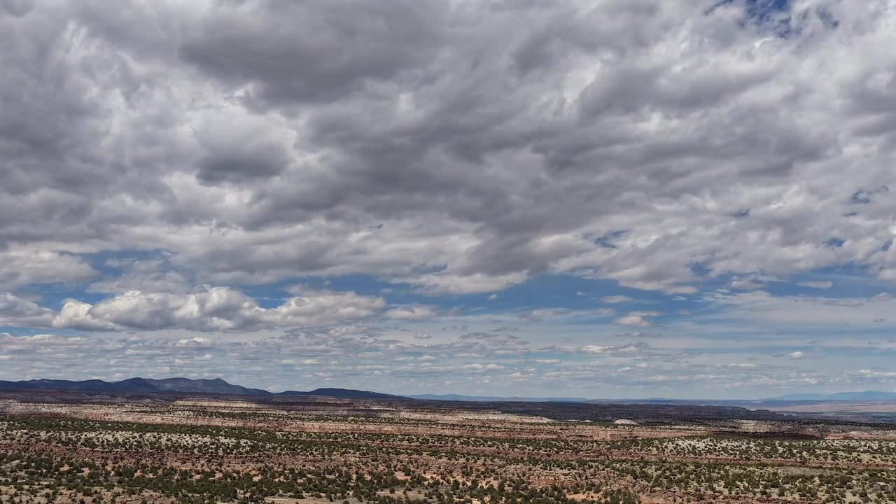 4K drone timelapse captures many layers of clouds shifting above desert mesas. Cinematic atmospheric motion reveals a rugged southwest landscape with a mountain range on the horizon.