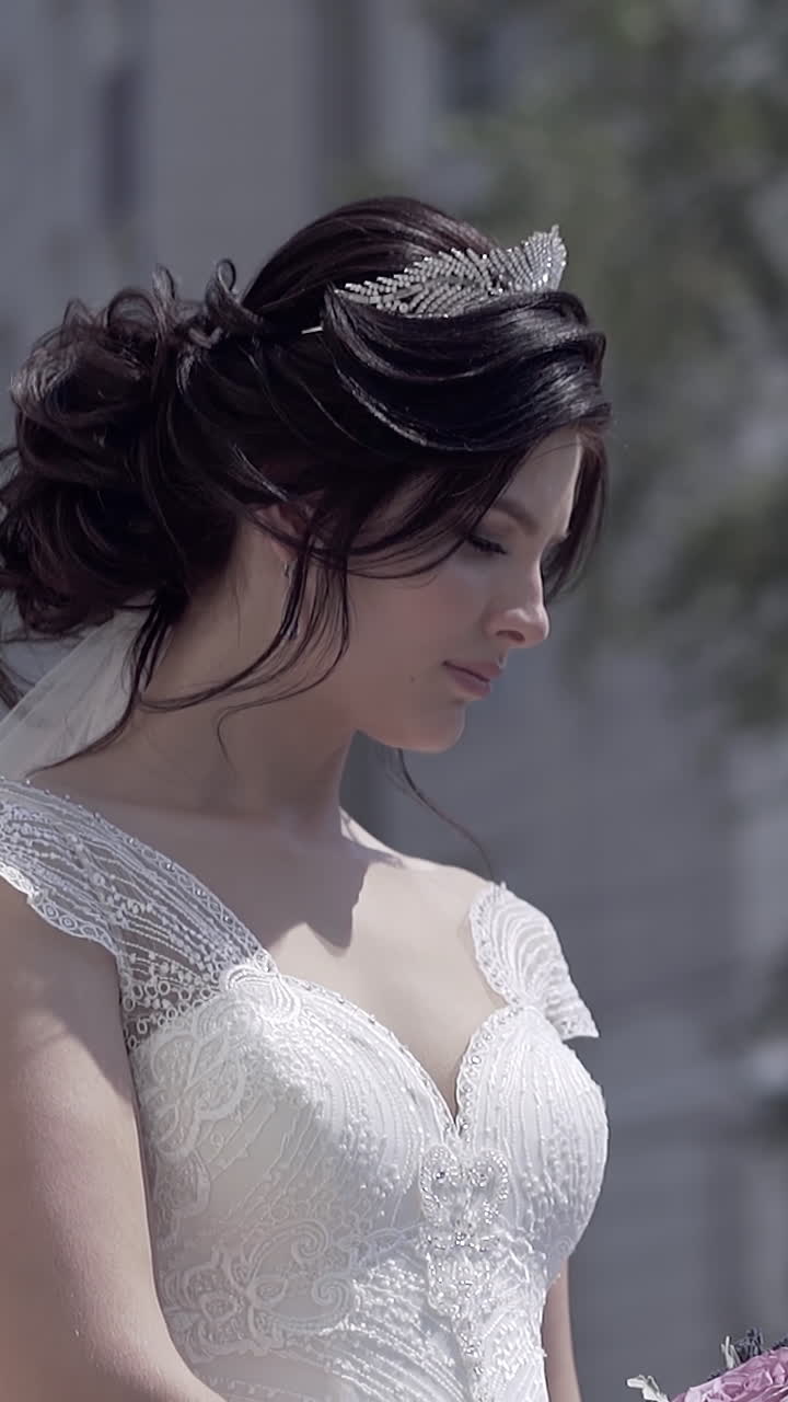 slow motion beautiful bride with tiara on brunette hair with white veil looks at bouquet and breathes deeply