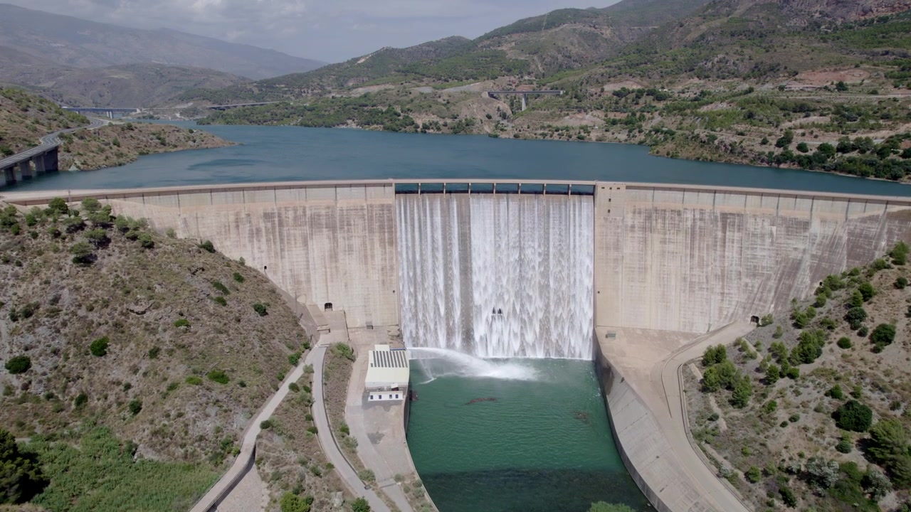Vandreservoir i fuld kapacitet. Dæmning frigiver vand, og vandkraftværk er i drift. Luftfoto med zoom ind. Rules-dæmningen. Spanien.