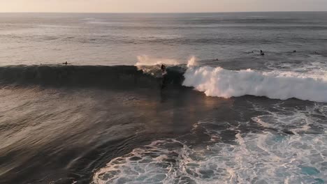 a drone flies over crashing waves as a surfer catches a wave at sunset on maui, hawaii's north shore near ho'okipa beach