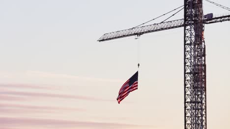 american flag hanging from crane waving in the breeze at dusk