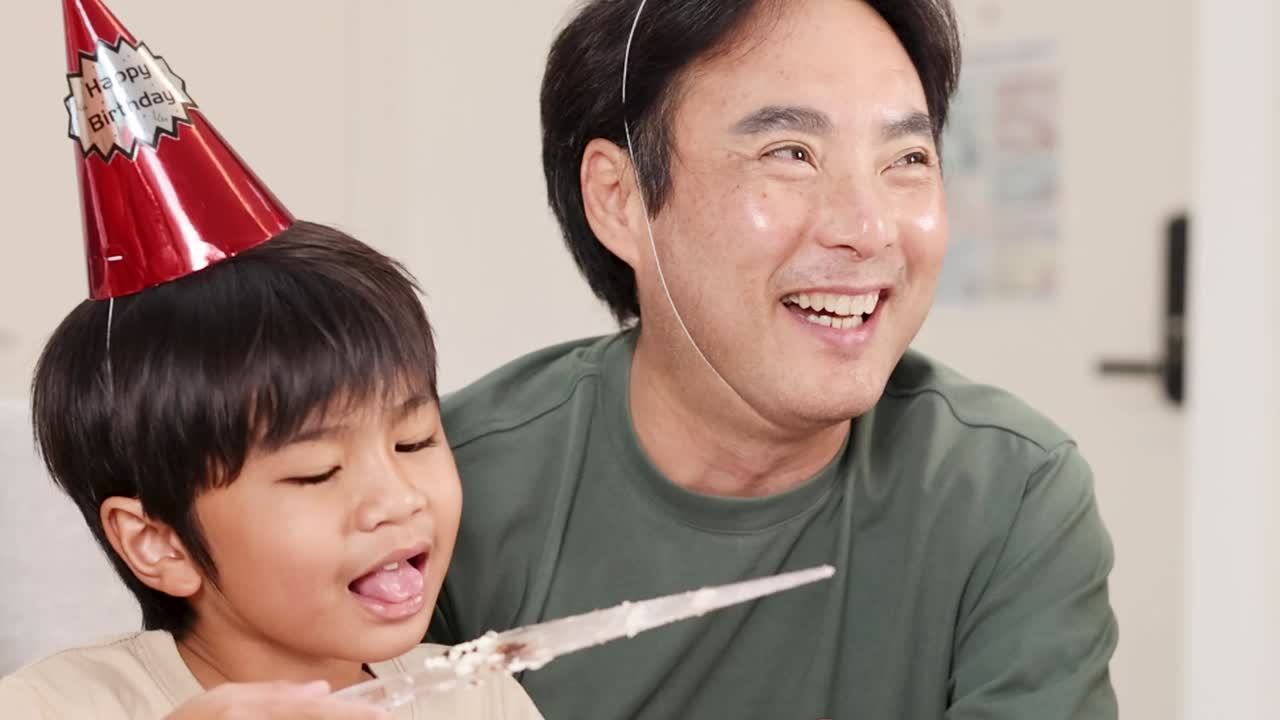 誕生日のお祝いの席で、パーティー帽子をかぶった父と息子が笑いながら遊んでいます。
