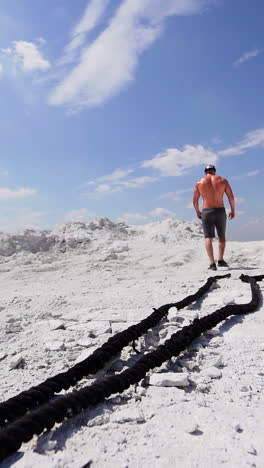 shirtless man in shorts going up after his workout with ropes outdoors. back view of a strong athlete rising on white mountain. vertical video