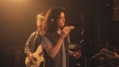 El-Vocalista-Hace-Movimientos-Visuales-Y-Canta-En-El-Micrófono-En-Un-Estudio-De-Grabación-De-Sonido.-Cantante-Adulto-Con-Banda-Musical-Graba-Nueva-Canción-En-Una-Habitación-Insonorizada.-Equipo-Musical-Profesional.-Producción-Musical.