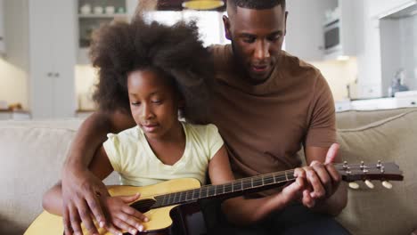 padre afroamericano y su hija sentados en el sofá tocando la guitarra juntos