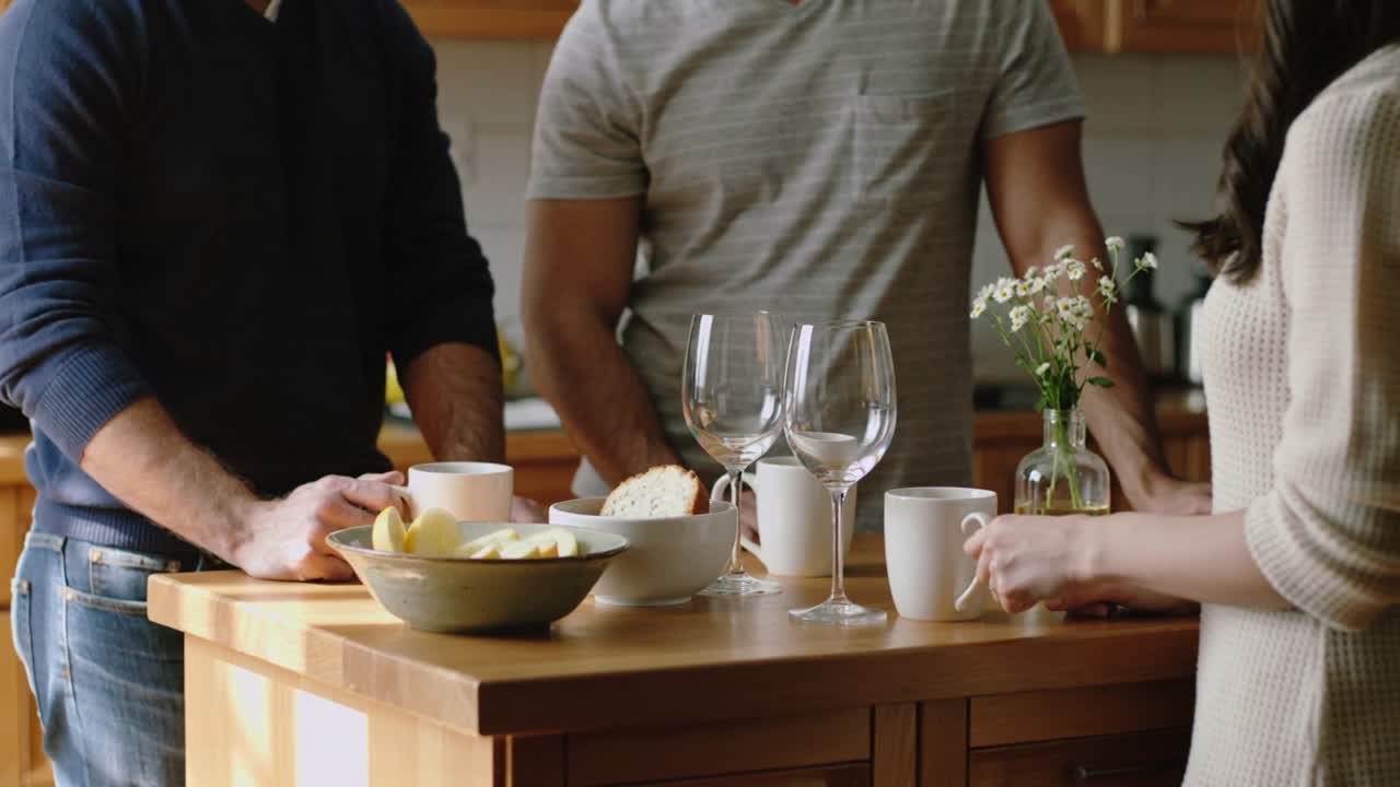 To mænd holder kopper, og kvinde placerer kop på trædisk, igangsætter hyggelig morgenkaffesnak.