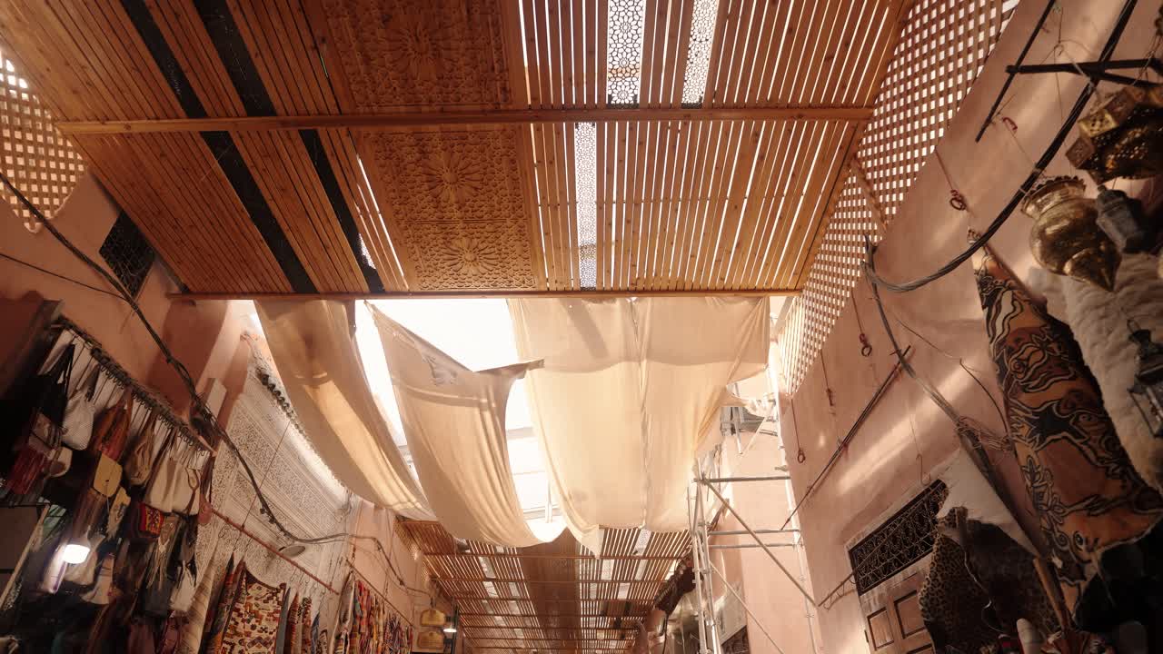 Wooden lattice roof and fabric canopies filter soft light above a traditional Moroccan market