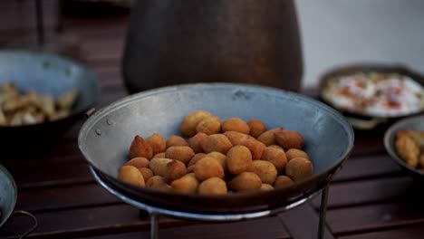 Round fried appetizers rest in a rustic tray during an outdoor catering or buffet event