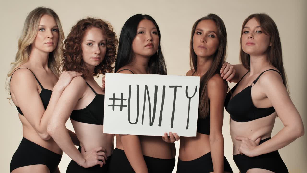 스튜디오에 서서 배너를 들고 있는 속옷을 입은 심각한 여성 그룹의 초상화.