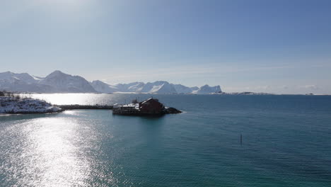 flying over isolated cabin during sunrise in quiet sea of senja island, norway