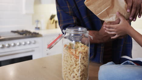 Mid section of happy biracial father and daughter unpacking shopping in kitchen, slow motion